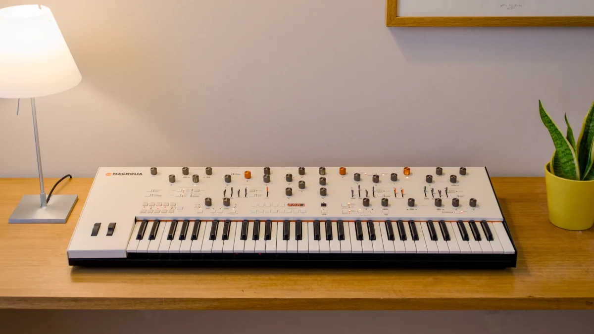 Magnolia analog FM synth launches Magnolia keyboard sitting on a wooden desk with a lamp and plant.